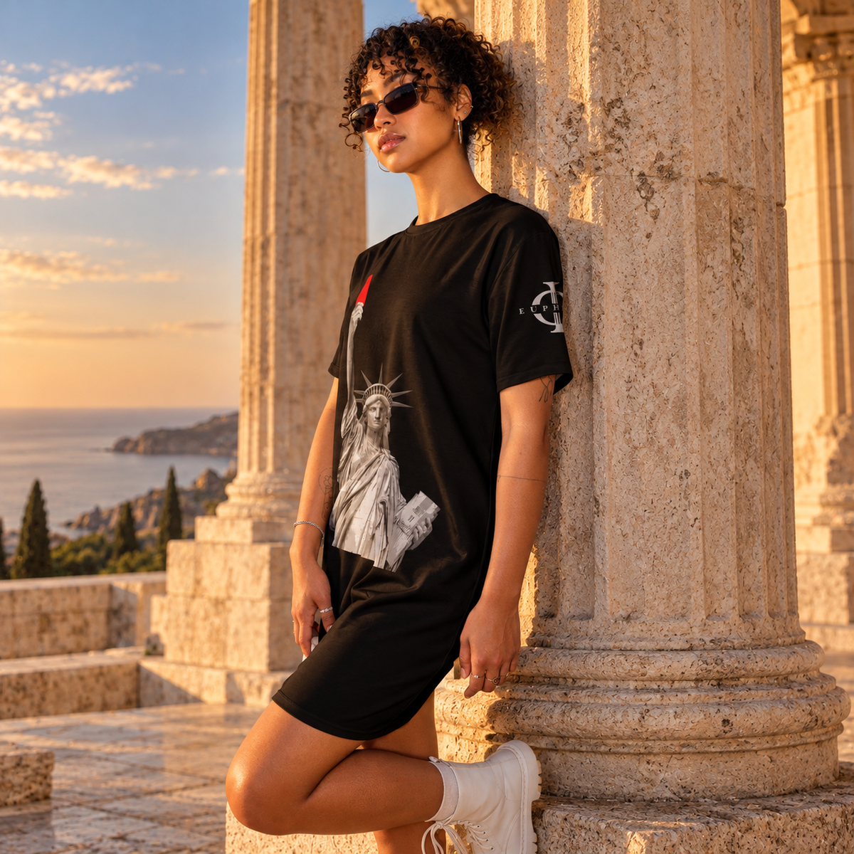 Collection Robes t-shirts Euphron : robe t-shirt noire Liberty's Red Card portée contre une colonne d'un temple grec face à la mer
